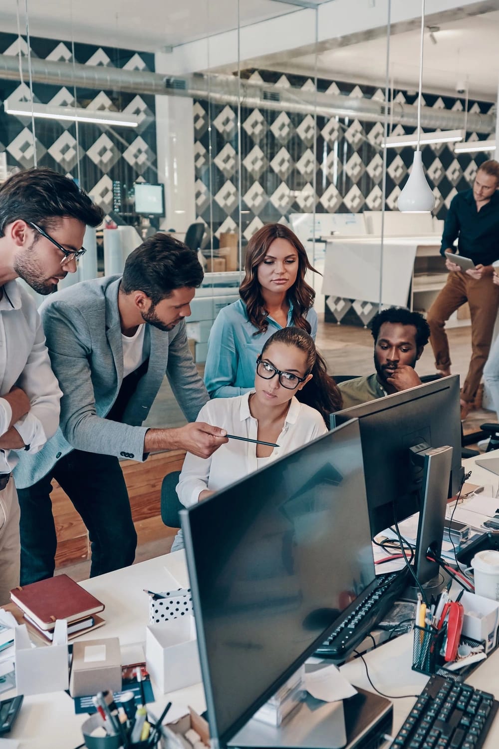 Diverse persone discutono tra loro davanti a dei monitor in un ufficio moderno e ben illuminato