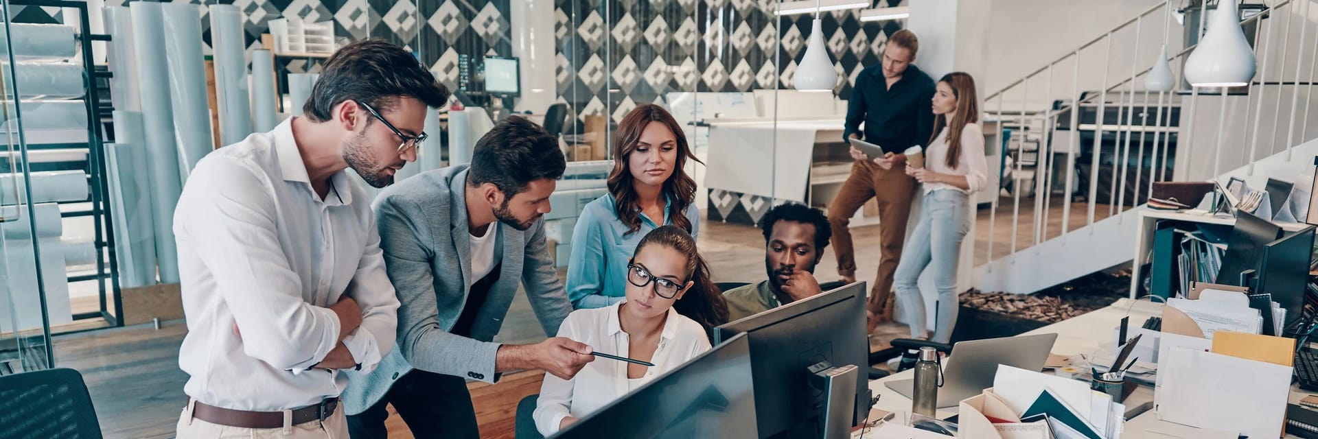 Diverse persone discutono tra loro davanti a dei monitor in un ufficio moderno e ben illuminato
